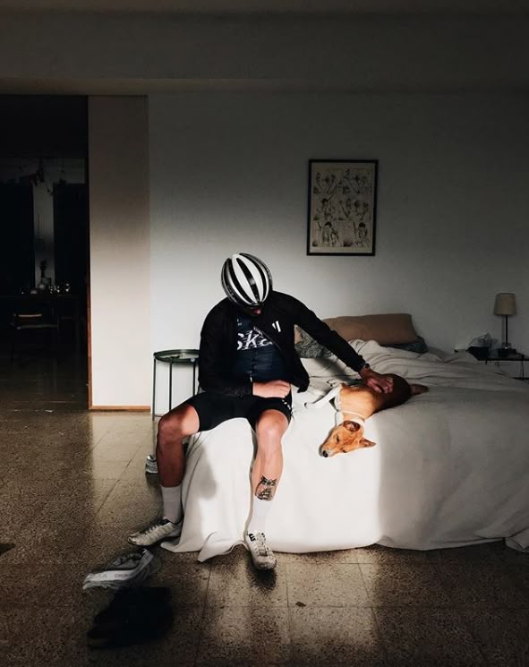 A rider seated in full kit on the edge of a bed in a lived-in room.