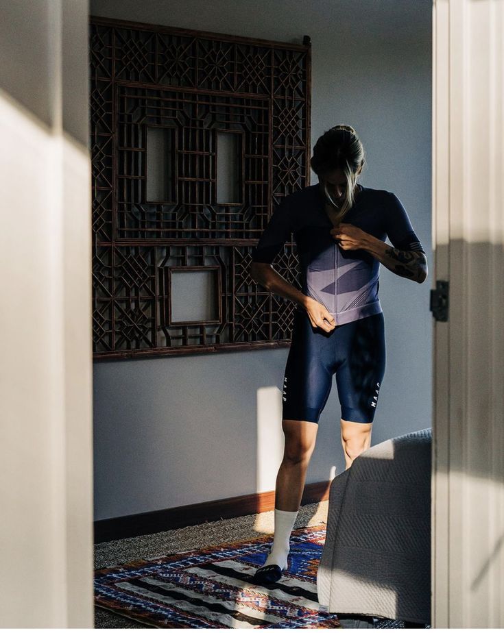 A rider adjusting their jersey while standing in doorway light.