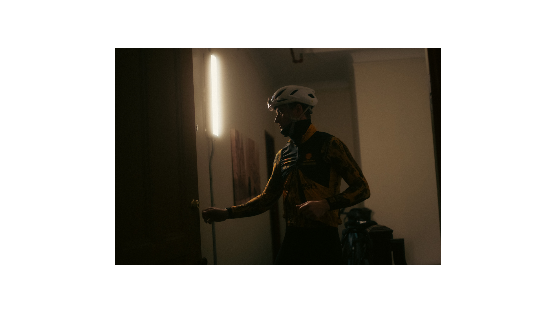 A cyclist in a doorway under hallway light before leaving.